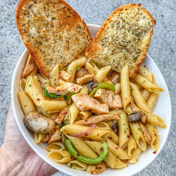 Penne pasta with chicken, mushrooms, green peppers, and two slices of garlic bread.