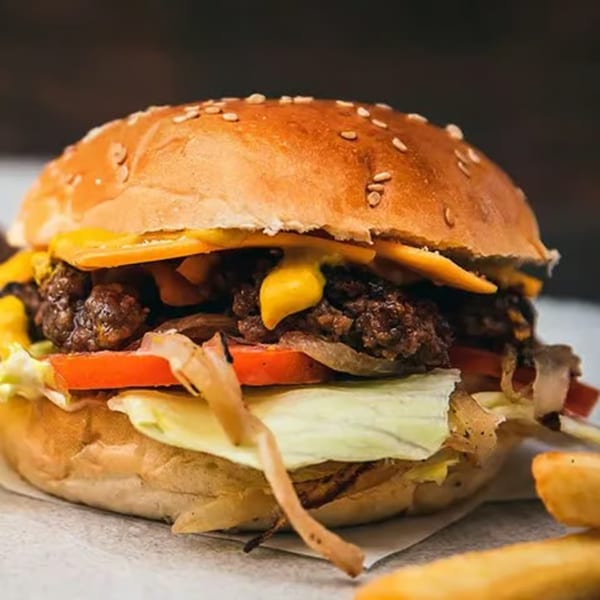 A close-up of a Milans Pizza & Wings burger with melted cheese, lettuce, tomato, and onions.