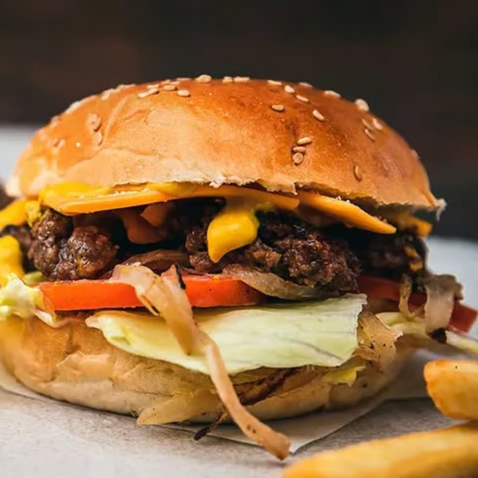 A close-up of a Milans Pizza & Wings burger with melted cheese, lettuce, tomato, and onions.