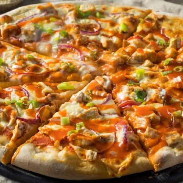 A close-up of a Milans Pizza & Wings buffalo chicken pizza with red onions and green onions.