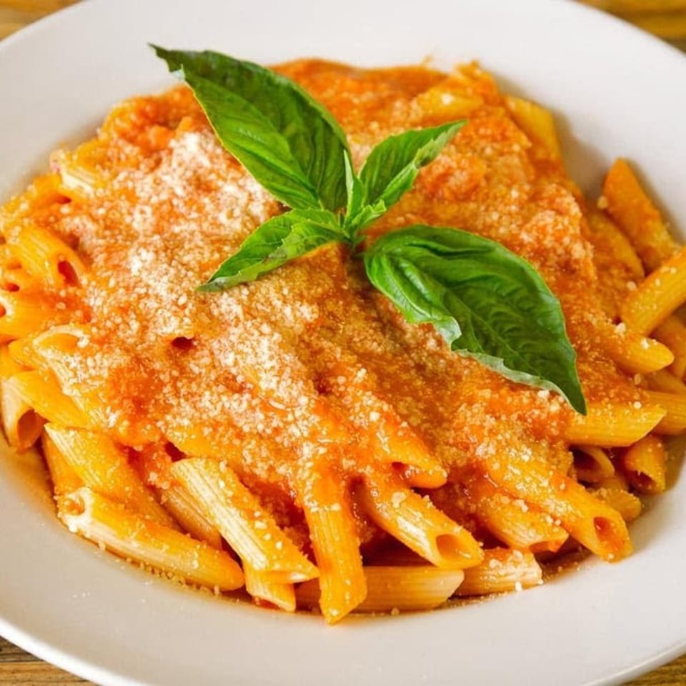Penne pasta with red sauce, parmesan cheese, and fresh basil on a white plate.