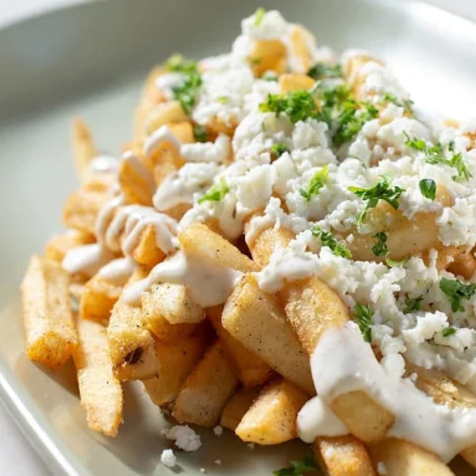Golden french fries topped with white cheese, creamy sauce, and fresh green herbs on a plate.