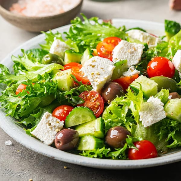 A vibrant Greek salad with lettuce, tomatoes, cucumbers, olives, and feta cheese.