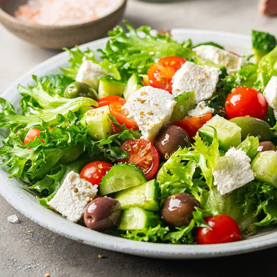 A vibrant Greek salad with lettuce, tomatoes, cucumbers, olives, and feta cheese.